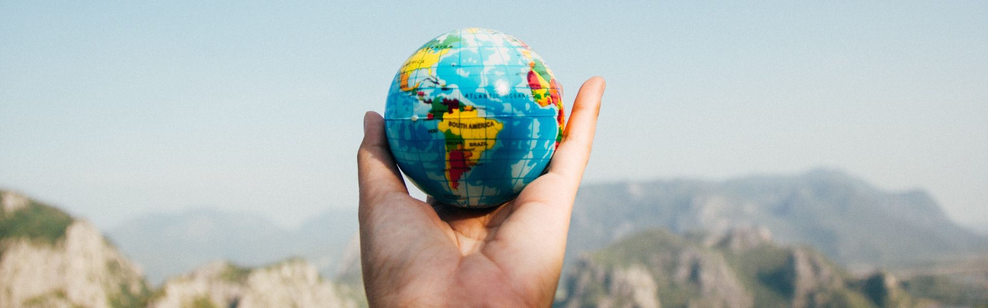 a hand holds a small globe with scenic view in background