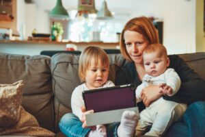 a mother sits with her young child during an online speech therapy session